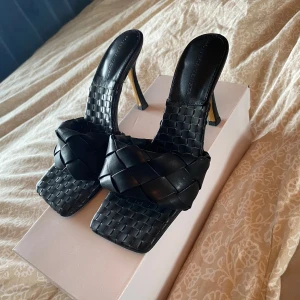 Svarta flätade höga sandaler. - Snygga svarta höga sandaler med flätad design i skinn. Skorna har fyrkantig tå, hög klack och bred rem över foten. Perfekta för dig som vill ha en trendig och lyxig look med statement-känsla. Köptes för 1000 kr. Passar 38-39
