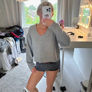 Grå stickad tröja - Supermysig grå croppad stickad tröja med v-ringning och långa ärmar. Perfekt till jeans eller kjol för en chill och stilren look. Tröjan har en loose passform och ribbade muddar vid ärmslut och nederkant.