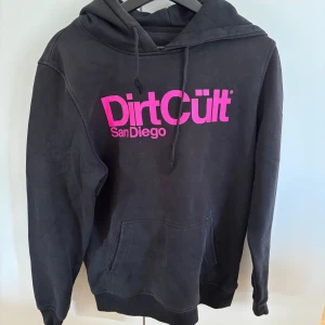 Svart Dirt Cult hoodie med rosa tryck - Svart hoodie från Dirt Cult med stor rosa logga, kan inte garantera att den är äkta, skriv vid frågor💘