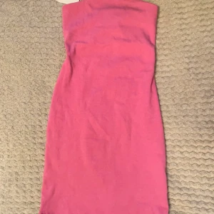 Rosa axelbandslös kortklänning - Snygg rosa axelbandslös kortklänning med tight passform. Perfekt för dig som vill sticka ut med en enkel men trendig look. Klänningen är ärmlös och har en rak, minimalistisk design.
