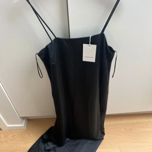 Navy långklänning Dagmar - Dagmar. Nypris 6000. Snygg mörkblå långklänning från Dagmar i glansigt material. Klänningen har tunna axelband och rak, minimalistisk siluett som ger en elegant look. Perfekt för dig som gillar stilren design och vill sticka ut med en klassisk vibe.