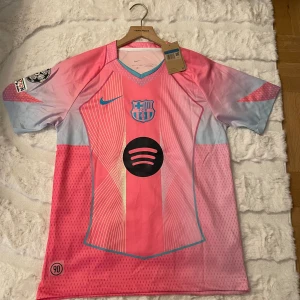 FC Barcelona rosa matchtröja Nike M - Säljer en helt ny FC Barcelona fotbollströja från Nike i storlek M. Tröjan är rosa med ljusblå detaljer, har klubbmärke och Nike-logga på bröstet samt Spotify-logga i svart. Tillverkad i lätt, ventilerande Dri-Fit-material och har korta ärmar. Perfekt för dig som älskar Barca och vill sticka ut. Aldrig använt nypris 1200 