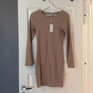 Beige ribbad klänning  - Snygg beige ribbad kortklänning med lång ärm och rund hals. Klänningen har en tight passform och är tillverkad i mjuk bomullsmix som sitter fint på. 
