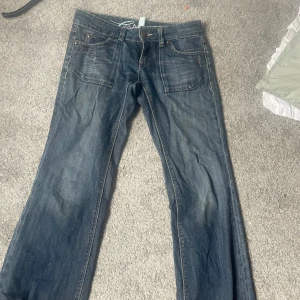Lågmidjade bootcut jeans från Esprit - Snygga blå jeans från Esprit med bootcut passform och coola detaljer på bakfickorna. Jeansen har klassisk femficksdesign, kontrastsömmar och är tillverkade i slitstarkt denim. Perfekta för dig som gillar en avslappnad men ändå trendig look.