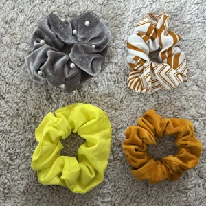 Fyra scrunchies i olika färger - Fyra scrunchies: en grå i sammet med pärlor, en vit och brun med randigt mönster, en knallgul i mjukt tyg och en senapsgul i sammet. Perfekta för att sätta upp håret med stil och färg.