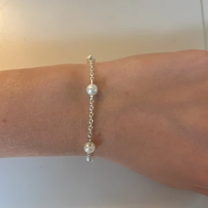 Silverarmband med pärlor - Ett stilrent armband i silverfärgad kedja med fem vita pärlor jämnt fördelade längs länken. Perfekt för dig som gillar en clean och elegant look. Justerbar längd med flera öglor för att passa olika handleder. Det är handgjort från C.S smycken.