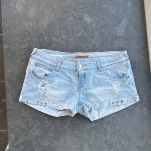 Ljusblå jeansshorts från Guess - Snygga ljusblå jeansshorts från Guess med slitna detaljer framtill. Klassisk femficksmodell och låg midja. Säljer då dom ej kommer till användning💞