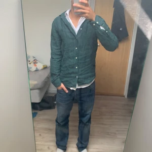 Grön linneskjorta från Riley  - Snygg grön skjorta i 100% linne med klassisk krage och knäppning framtill. Skjortan har lång ärm, perfekt för dig som gillar en stilren men chill look. Passar bra till jeans eller chinos.
