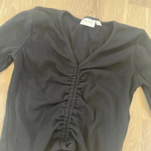 Svart ribbad topp från Gina Tricot - Svart långärmad topp från Gina Tricot med ribbad struktur och snygg snörning framtill som ger en cool rynkad effekt. V-ringad och croppad modell som passar perfekt till jeans eller kjol. Enkel att styla och superbekväm, samt stretchig. Såååå himla söt!!😍💘