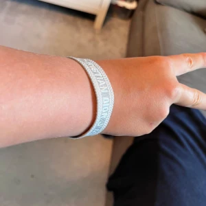 Grått Christian Dior armband - Snyggt vävt armband från Christian Dior i ljusgrått med vit broderad logga. Armbandet har justerbar knytning med tofsar i ändarna och ger en trendig och stilren vibe. Perfekt accessoar för att lyfta din outfit.