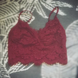 Vinröd spetsig korsett-topp - Supersnygg vinröd korsett-topp i spets med blommigt mönster. Toppen har smala axelband, v-ringning och dragkedja bak. Perfekt för att lyfta vilken outfit som helst med sin romantiska vibe och detaljerade spetskant.