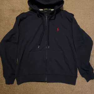 Marinblå Ralph Lauren Zip hoodie - Medium - Marinblå hoodie med dragkedja och röd logotyp på bröstet. Modellen är "Custom Fit". Använd 4 gånger, tvättad i efterhand