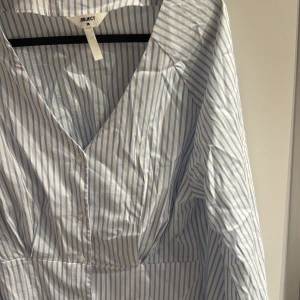 Blåvit skjorta från Object - Snygg blåvit randig skjorta med framhäven midja från Object med v-ringning och knappar framtill. Skjortan långa ärmar och smock i ryggen för en bekväm passform. 