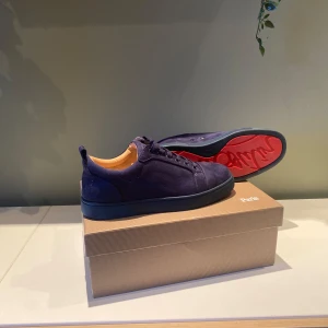 Mörkblå sneakers från Louboutin - Snygga mörkblå sneakers från Christian Louboutin i mocka med klassisk röd sula och diskret logga på sidan. Skorna har rund tå, snörning och beige innersida. Perfekta för dig som vill sticka ut med exklusiva detaljer. Følger med alle tilbehør som tilhører kjøp fra Christian Louboutin!