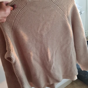 Beige ribbstickad tröja - Säljer en beige ribbstickad tröja med rund hals och lång ärm. Tröjan har en relaxed passform och är perfekt för lager-på-lager. Materialet känns mjukt och ger en chill vibe till outfiten. I slutet har den lite slit på båda sidorna
