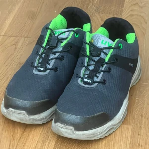 Uvex svarta sneakers med gröna detaljer - Bekväma och lätta skyddsskor från Uvex i sportig design. Använda men i gott skick. ✔️ Uppfyller EN ISO 20345 (S1P) ✔️ Tåhätta i komposit – lätt och stark ✔️ Halksäkra sulor (SRC) ✔️ ESD-skydd (antistatisk) ✔️ Snabbsnörning för enkel användning ✔️ Andningsbart material – perfekt för långa arbetsdagar