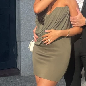 Olivgrön omlott kortklänning - Säljer en olivgrön kortklänning med snygg omlott-drapering över bysten och axelbandslös design, möjligt att ta upp axeln då jag gömt den på bild. Klänningen har en figurnära passform och är perfekt för dig som gillar stilrena och trendiga plagg. Materialet känns mjukt och följsamt mot kroppen. Pris kan diskuteras!💚