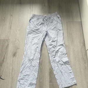 Randiga linnebyxor med snörning  - Lätta och luftiga linnebyxor från lager 157 i storlek S. Byxorna har smala blå och vita ränder, elastisk midja med snörning och raka ben. 