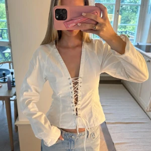Vit snörad blus från Zara - Supersnygg vit skjorta från Zara med lång ärm och djup v-ringning. Framsidan har cool snörning hela vägen ner. I jeans material