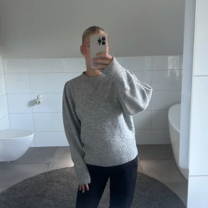Grå stickad tröja med puffärm H&M - Mysig grå stickad tröja från H&M med puffiga ärmar och bred ribbad mudd vid ärmslut och nederkant. Tröjan har en klassisk rund halsringning och en loose fit som ger en chill vibe. Perfekt för lager-på-lager under kyliga dagar.