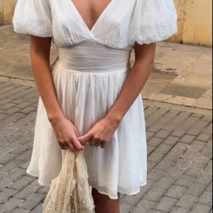 Student klänning vit med rosett från Gina Tricot - Supersöt vit kort klänning från Gina Tricot med puffiga korta ärmar, djup v-ringning och stor rosett i ryggen. Perfekt till studenten/skolavslutning mm. ALDRIG ANVÄND.