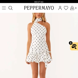 Vit prickig miniklänning från PepperMayo - Supersöt vit miniklänning med svarta prickar från PepperMayo. Asymmetrisk hals med scarf-detalj, omlott vid axeln och volangkant nertill. 