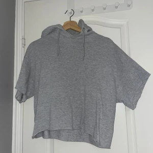 Grå hoodie med kort ärm - Säljer en grå hoodie med avklippta ärmar och luva med snören. Perfekt för dig som gillar att ha något bekvämt och snyggt till ett par jeans. Materialet känns mjukt och lätt. Storlek S. Varan säljs på flera plattformar💕