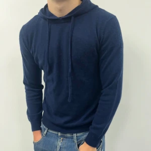 Marinblå hoodie i kashmir & merinoull  - Snygg marinblå hoodie i mjukt material . Tröjan har huva med snörning och långa ärmar, samt ribbade muddar vid ärmslut och nederkant. Perfekt för dig som gillar stilren och skön design med premiumkänsla.