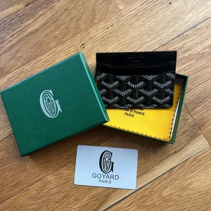 Goyardplånbok - Säljer en stilren svart plånbok med deras ikoniska grafiska mönster i vitt och grått. Plånboken är tunn och smidig, perfekt för kort och sedlar. Kommer med original ask, tygpåse och äkthetskort. Riktigt snygg accessoar för dig som gillar lyxiga detaljer.