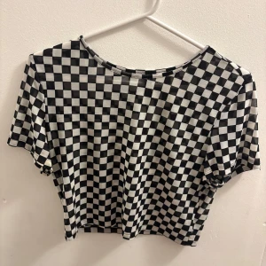 Svartvit rutig croppad topp H&M Divided - Säljer en croppad topp från H&M Divided med svartvitt rutigt mönster. T-shirten har korta ärmar och rund halsringning. Perfekt för dig som gillar streetstyle och vill sticka ut med ett coolt mönster.