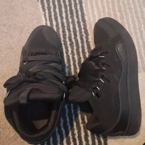 Svarta chunky sneakers med bred snörning - Säljer ett par svarta chunky sneakers med breda snören och högt skaft. Skorna har en cool, sportig vibe med detaljer i syntet och mesh för extra andningsförmåga. Perfekta för dig som gillar streetstyle och vill sticka ut med dina skor.