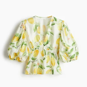 Vit blommig blus med citronmönster - Superfin blus i vitt med färgglatt citronmönster och gröna blad. Den har v-ringning, puffiga trekvartsärmar och smockad midja som ger en snygg siluett. Perfekt för dig som vill sticka ut med en fräsch och somrig vibe.