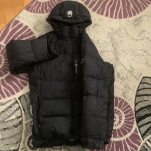 Svart Sail Racing dunjacka med huva - Svart skal racing jacka Storlek M.         Jackan är använd i 1år men är i helt okej skick. Har några små hål men de märks knappt här inte fått en ända kommentar om dem. Pris kan diskuteras. Passar till S M och kanske L