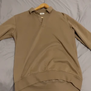 Beige pikétröja från Kappahl - Säljer en beige pikétröja från Kappahl med klassisk krage och knappslå. Tröjan har långa ärmar och ribbade muddar vid ärmslut och nederkant. Perfekt för dig som gillar enkel och stilren design. Materialet känns mjukt och skönt mot huden. Storlek 170