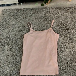 Ljusrosa linnetopp med smala axelband - Supersöt ljusrosa linnetopp med smala axelband och enkel, clean design. Toppen är ärmlös och har en rak, något tight passform som sitter snyggt mot kroppen. Perfekt att styla med jeans eller kjol för en chill look.