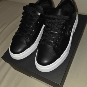 Philipp Plein svarta sneakers strl 43 - Svarta Philipp Plein sneakers i skinn med chunky vit sula och svarta snören. Sidan pryds av en metallogo och detaljer i silver. Klassisk low-top modell med rund tå och stilren design, perfekt för dig som gillar exklusiva streetwear-vibbar. Hell oanvända