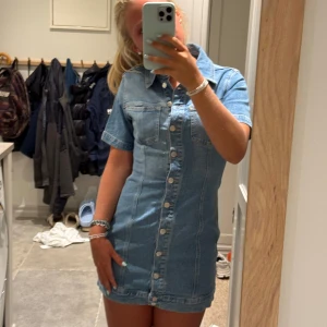 Kort jeansklänning med knappar - Säljer en snygg kort jeansklänning i ljusblå denim med korta ärmar och krage. Klänningen har framfickor på bröstet och hela knappraden framtill. Köpt på zara i storlek M. 