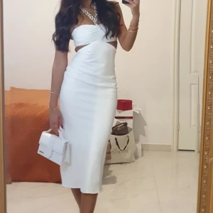 Vit axelbandslös långklänning - Snygg vit axelbandslös långklänning med cut out-detaljer i midjan och figurnära passform. Klänningen har en stilren look och är perfekt för dig som vill sticka ut. Materialet känns slätt och stretchigt, och modellen är ärmlös med en elegant siluett.