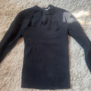 Svart topp från Zara - Svart stickad polotröja från Zara med lång ärm och cool half zip-detalj vid halsen. Tröjan har en modern, slim passform och är perfekt för dig som gillar stilrena och minimalistiska plagg. Materialet är mjukt och stretchigt, vilket gör den skön att bära. Liten defekt se bild 2
