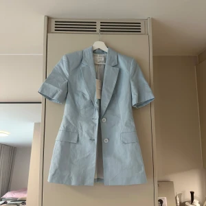 Ljusblå kavaj med kort ärm från NA-KD - Snygg ljusblå kavaj från NA-KD med korta ärmar och två knappar framtill. Ny med lappen kvar! Slutsåld! Köpt för 600kr💗