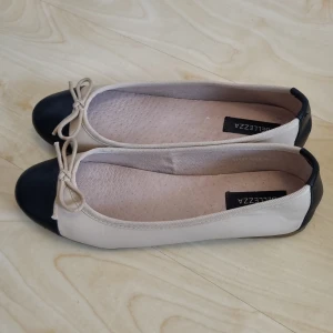 Beiga ballerinaskor med svarta detaljer - Snygga ballerinaskor från Bellezza i beige med svarta detaljer på tå och häl. Skorna har en klassisk rund tå, liten rosett framtill och platt sula. Tillverkade i syntetmaterial. Köpta på Vinted för runt 200 kr. Använda en gång, samt få gånger av förra ägaren men i bra skick. OBS, skorna är en mörkare beige än på bilderna. Vet inte exakt vilket märke de är ifrån från början. 