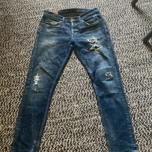 Blå skinny jeans från George - Säljer ett par blå skinny jeans från Dundup model  George med slitna detaljer och snygga slitningar på benen. Jeansen har klassisk femficksdesign, orange sömmar och är tillverkade i stretchigt denim för en tight passform. Storlek 35 sitter som 34. Midjemått 43cm och längd 106cm.Kan gå ner i pris vid snabb affär