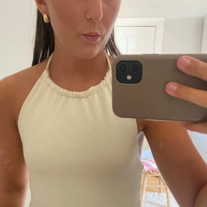 Beige halterneck linnetopp - Säljer en beige halterneck linnetopp med smala band som knyts i nacken och öppen rygg. Mjuk och stretchig känsla, superenkel att matcha med jeans eller kjol. Köpt från NA-KD och använt få tak gånger, så som ny💕