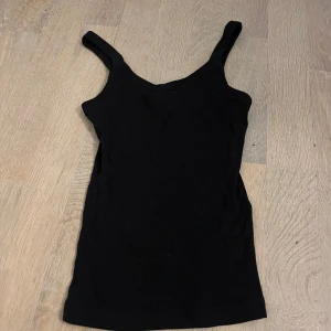 Svart ribbad linnetopp Gina Tricot - En svart ribbad linnetopp från Gina Tricot, basically basics-kollektionen. Toppen har breda axelband och är figurnära med stretchigt material. 