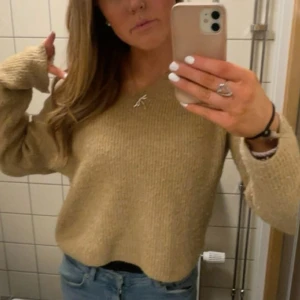 Beige stickad tröja med v-ringning - Säljer en beige stickad tröja med v-ringad hals och långa ärmar. Tröjan har en loose passform och är perfekt att matcha med jeans. Mjuk och skön känsla, passar dig som gillar enkel och stilren look.