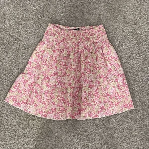 Blommig rosa kortkjol från Gina tricot  - Supersöt kortkjol från Gina tricot med blommigt mönster i rosa, vitt och lite gult. Kjolen har smock i midjan och volangdetaljer som ger extra flow. Perfekt för vår och sommar, lätt och luftig i bomullsmaterial.