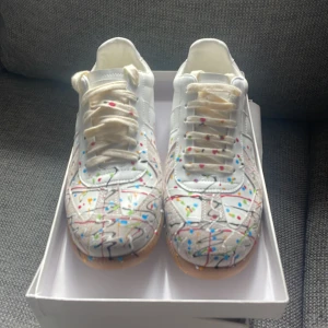 Maison Margiela sneakers med färgstänk - Unika vita sneakers från Maison Margiela med coola färgstänk i blått, rött, grönt, gult och svart. Passar storlek 42, har tyvärr inget kvitto pris ej hugget i sten. Säljer för dem för att de va fel storlek 