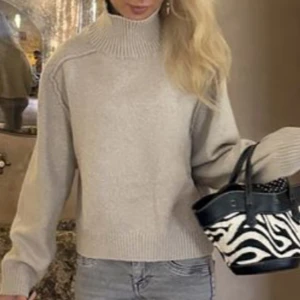 Beige stickad polotröja - Säljer en beige stickad polotröja med hög, ribbad krage och långa ärmar. Tröjan har en loose passform och är perfekt för dig som gillar enkel och stilren look. Passar XS-S! 