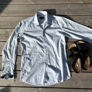 Ljusblå randig skjorta från Eton - Säljer en stilren ljusblå skjorta från Eton i storlek 39, slim fit. Skjortan har diskreta tunna ränder, klassisk krage och vita knappar. Tillverkad i 100% bomull och passar perfekt till jeans eller chinos för en clean look. Nypris ligger på 1800kr