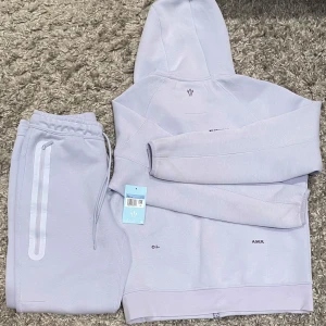 Nike NOCTA ljuslila mjukisbyxor - Säljer ett par ETT AV ETT stilrena ljuslila mjukisbyxor från Nike NOCTA med elastisk midja och dragsko. Byxorna har raka ben, diskreta fickor med dragkedja och NOCTA-logga på benet. Perfekta för chill eller träning, riktigt clean look. PRISET KAN DISKUTERAS.